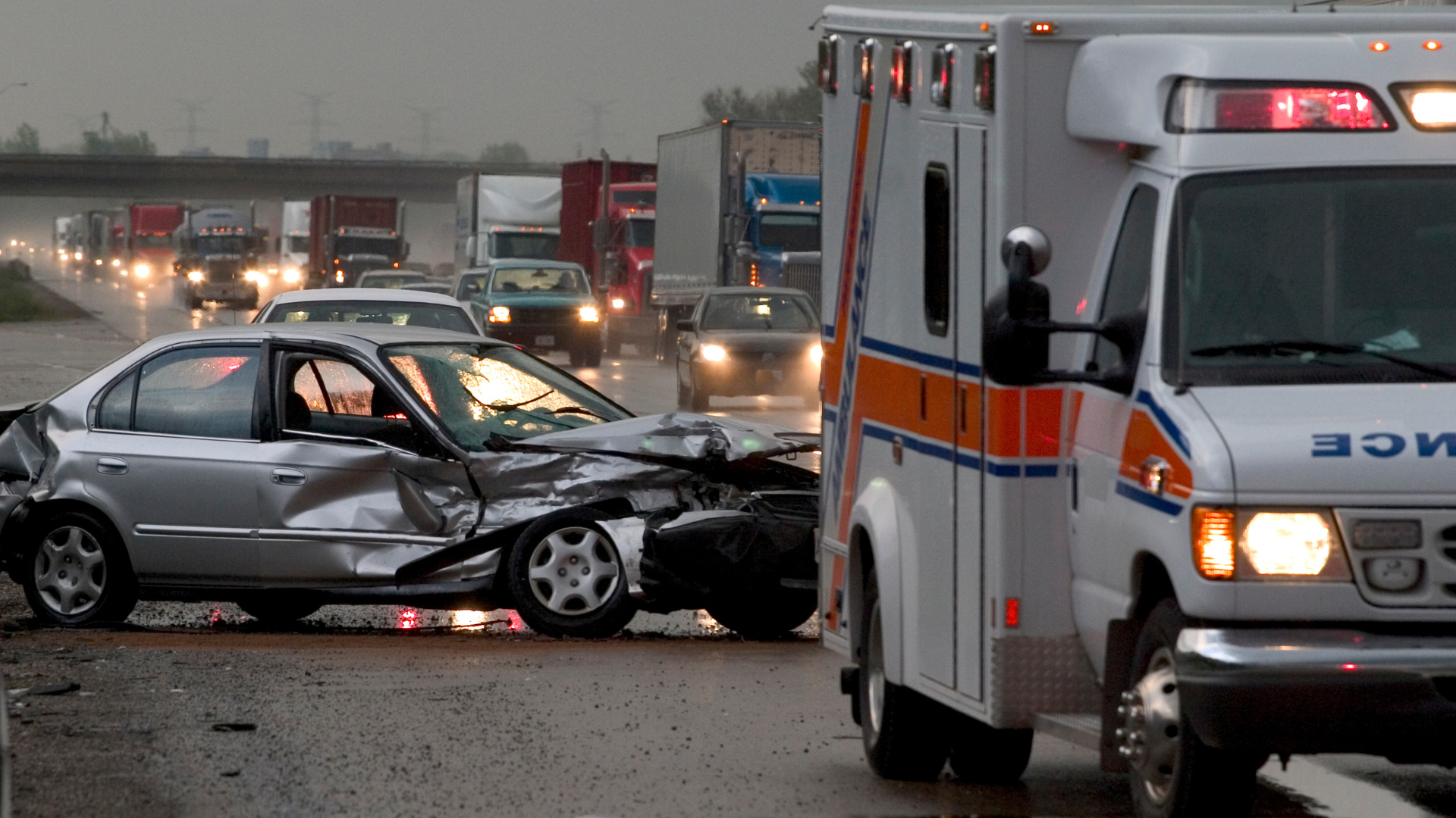 Ambulance and damaged silver car on a rainy Seattle highway after a collision, representing emergency response to car accidents.